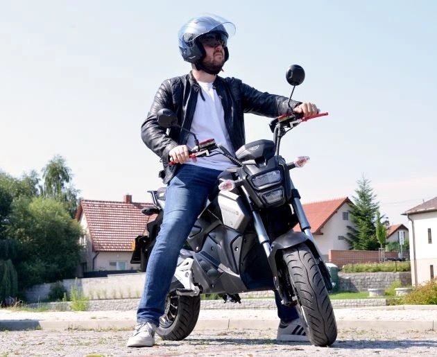 Muž s helmou hľadí do diaľky a sedí na stojacom elektrickom motocykli HECHT STRATIS