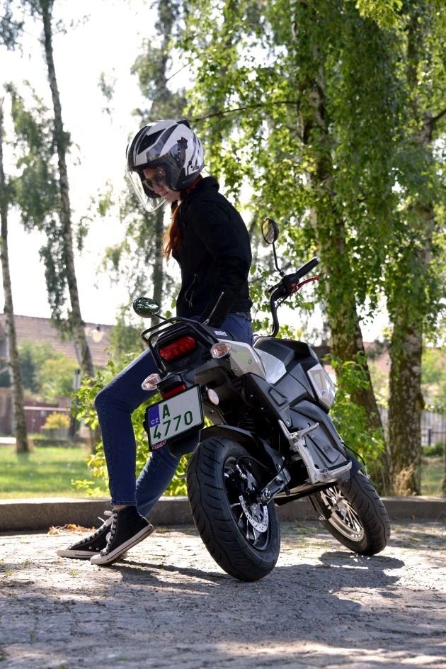 Žena s helmou opretá o stojaci elektrický motocykel HECHT STRATIS