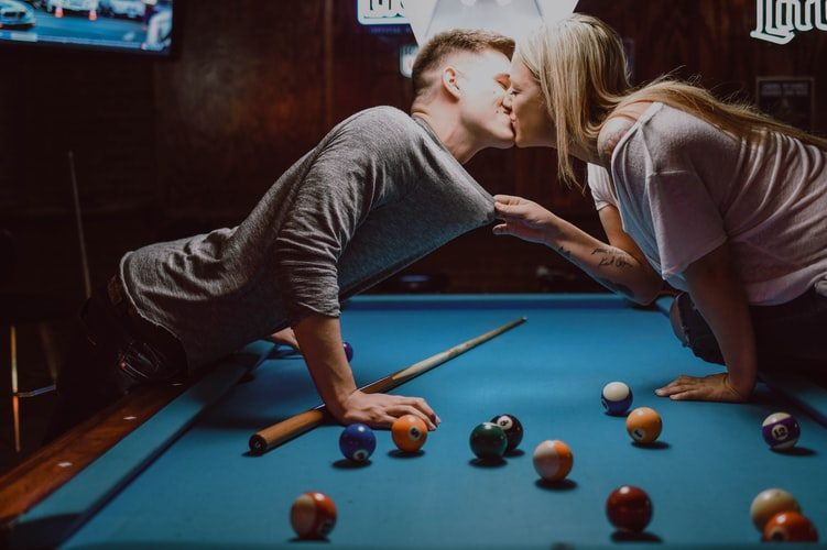žena a muž hrajú biliard a bozkávajú sa pri tom