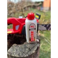 Olej na mazanie reťazí položený na pni a v pozadí píla HECHT 2039