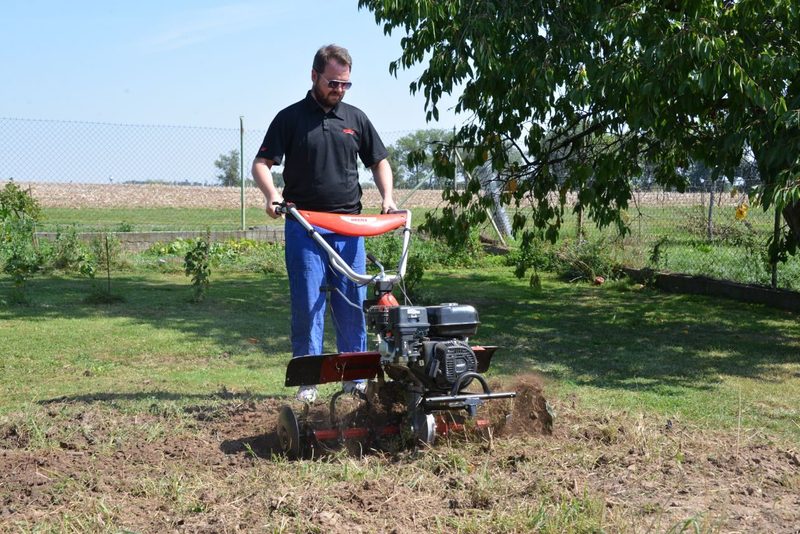 muž pracujúci s benzínovým kultivátorom na záhone
