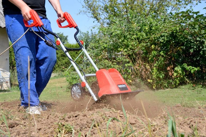 Muž držiaci elektrický kultivátor v plnom nasadení v záhone