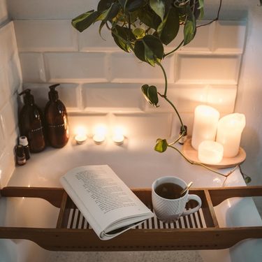 domáci wellness, zapálené vonné sviečky, kniha, drevený podnos do vane, šálka čaju