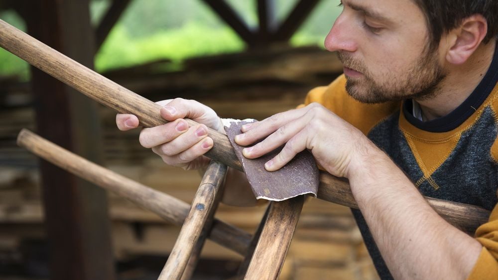Ruční broušení dřeva smirkovým papírem při odstraňování starého nátěru