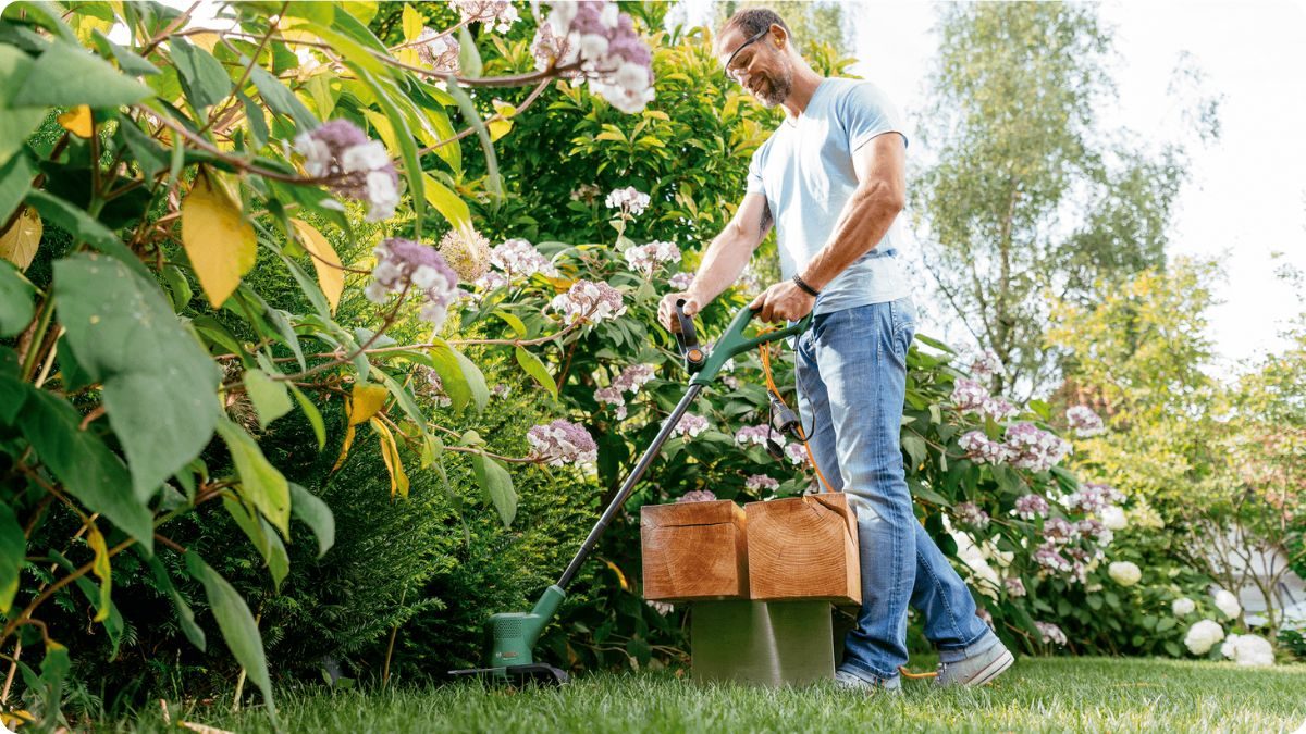 Strunová sekačka při údržbě okrajů trávníku kolem záhonů na zahradě