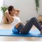 Žena cvičiaca pilates s modrým overballom Sportago pod chrbátom na modrej podložke.