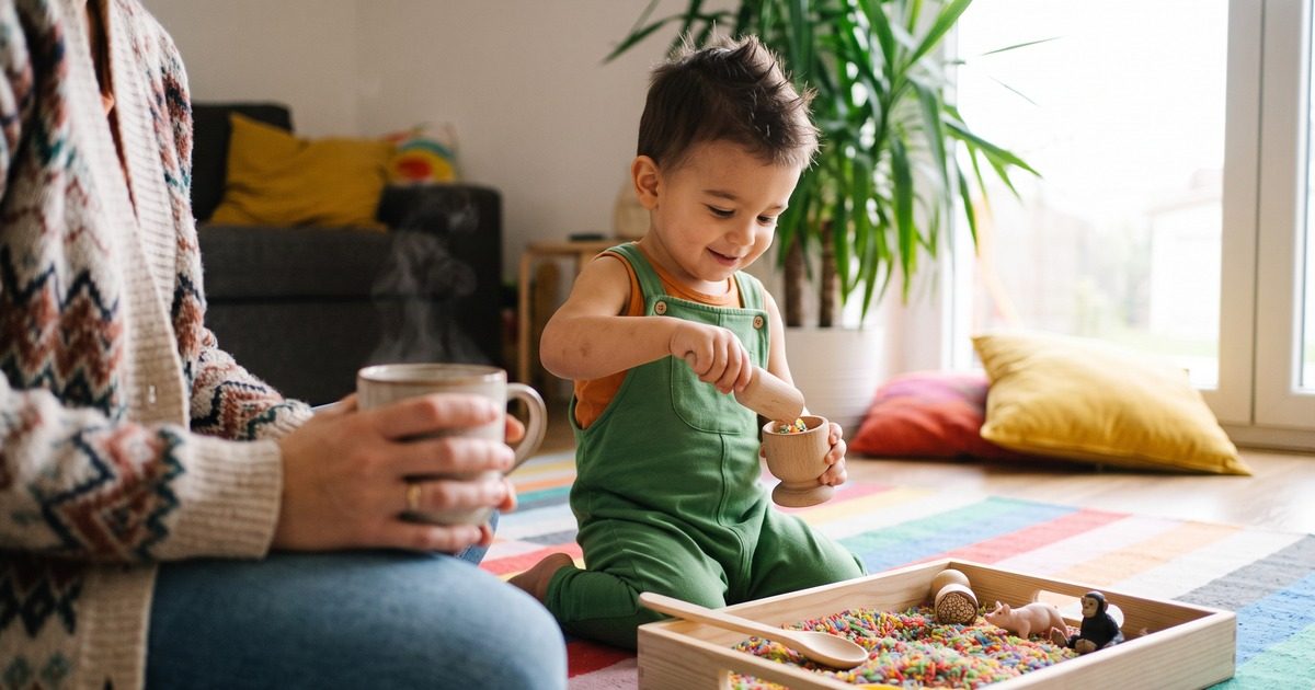 Batole přesýpá duhovou rýži v Mém prvním smysloboxu, máma pije kávu